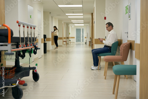 Man in glasses sits in a hospital corridor with a phone in his hands