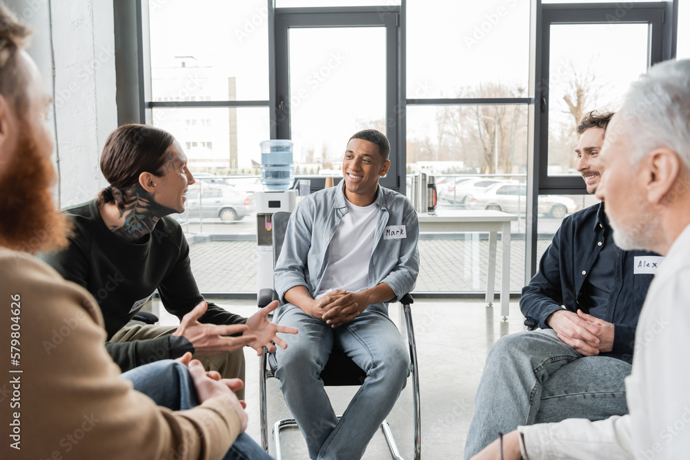 Tattooed man with alcohol addiction talking to multiethnic group in rehab center. Tattooed man with alcohol addiction talking to multiethnic group in rehab center.