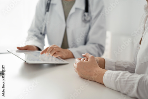 Doctor and patient discussing current health examination while sitting at the desk in clinic office. The focus is on female patient's hands, close up. Perfect medical service and medicine concept.