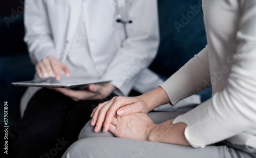 Doctor and patient sitting at sofa in clinic office. The focus is on female woman s hands  close up. Medicine concept
