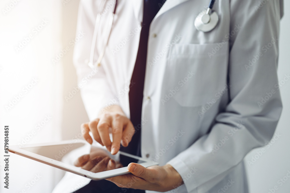 Doctor woman using tablet computer while standing near panorama window in clinic, close up. Physician or surgeon at work. Medicine concept. Doctor woman using tablet computer while standing near panorama window in clinic, close up. Physician or surgeon at work. Medicine concept.