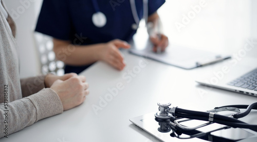 Stethoscope lying on the tablet computer in front of a doctor and patient at the background. Medicine, healthcare concept.