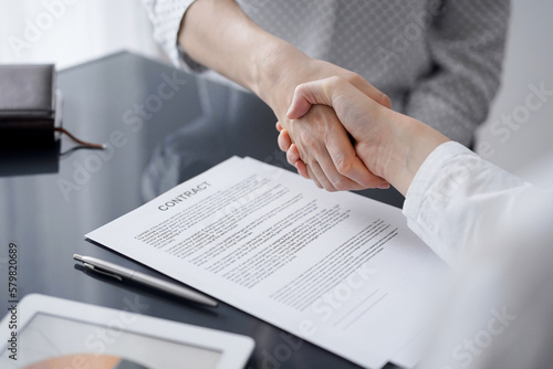 Business people signing contract papers while sitting at the glass table in office, closeup. Partners or lawyers working together at meeting. Teamwork, partnership, success concept.