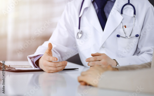 Unknown male doctor and patient woman discussing something while sittingin a darkened clinic, glare of light on the background. Close-up of hands photo