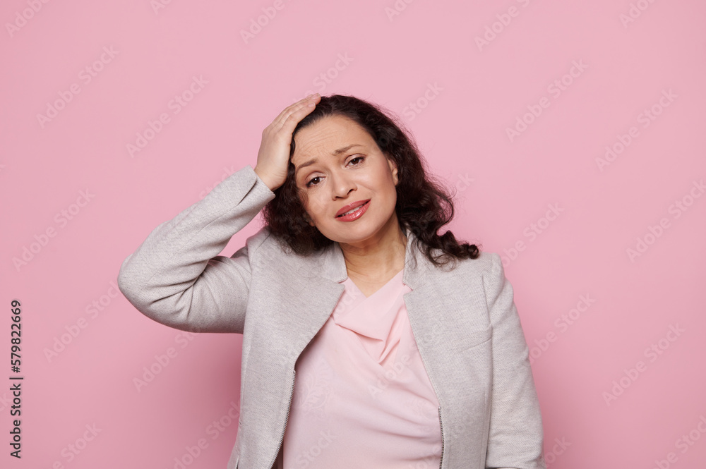 Overworked multitasking woman, businesswoman, manager suffers from tension headache, holding hand on her head, looking at camera with desperate look and hopeless, isolated over pink color background Overworked multitasking woman, businesswoman, manager suffers from tension headache, holding hand on her head, looking at camera with desperate look and hopeless, isolated over pink color background