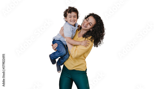 Happy young curly hispanic woman in casual clothes lifts up ;little son smiling standing against transparent background. Cheerful caucasian brunet kid embracing excited mother.