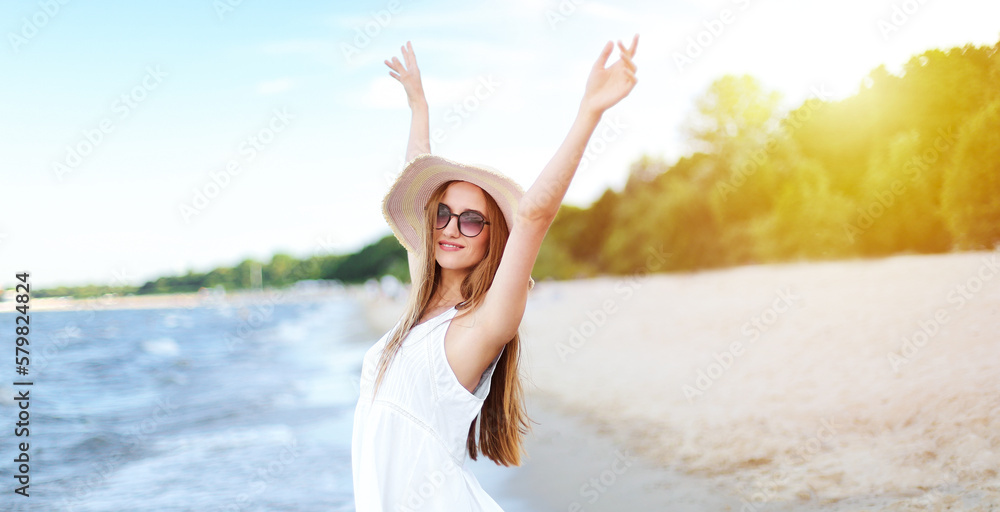 Happy smiling woman in free happiness bliss on ocean beach standing with a hat, sunglasses, and rasing hands. Portrait of a multicultural female model in white summer dress enjoying nature Happy smiling woman in free happiness bliss on ocean beach standing with a hat, sunglasses, and rasing hands. Portrait of a multicultural female model in white summer dress enjoying nature