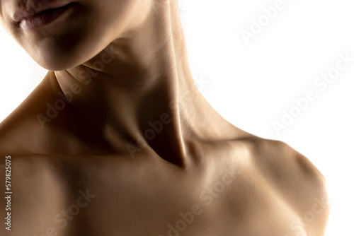 The close-up of a young woman's neck and shoulders in the shadow on white studio background