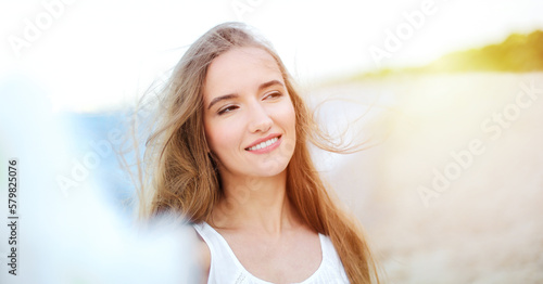 Portrait of a happy smiling woman in free happiness bliss on ocean beach enjoying nature during travel holidays vacation outdoors. View through white blurred flowers.