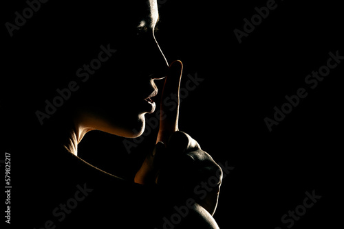 Φωτογραφία Silhouette of unknown woman with the face in the shadow holding finger on her li