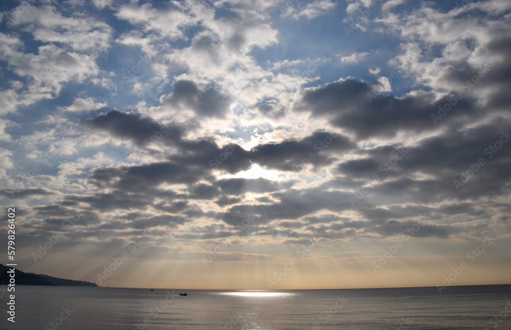 Sun rays pass through clouds over the sea.