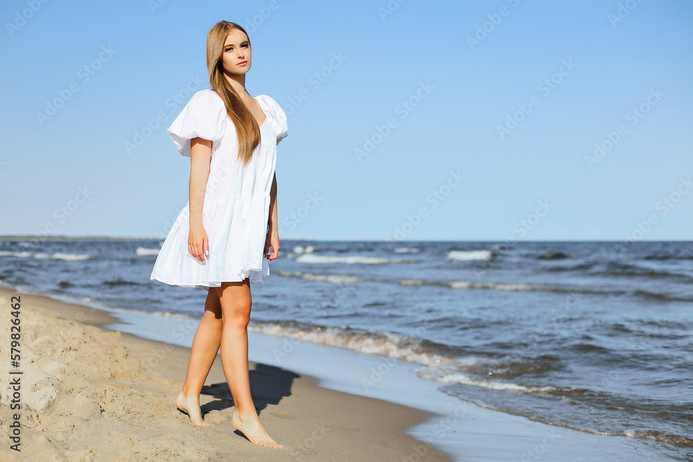 Happy smiling beautiful woman is walking on the ocean beach in a white summer dress. Happy smiling beautiful woman is walking on the ocean beach in a white summer dress.