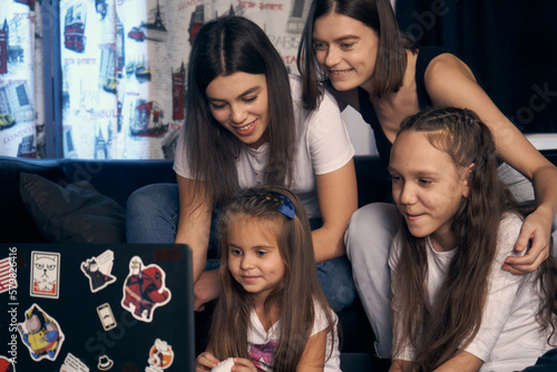 Staged photo. A lesbian couple and their children are having a good time at home. The whole family gathered around the screen watching cartoons. The girls are having a lot of fun.