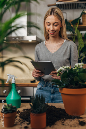 Woman is surrounded by houseplants and she is using tablet