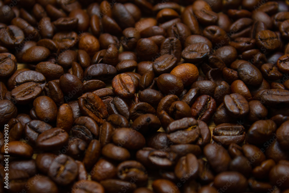 Fascinating background of roasted coffee beans. Fragrant roasted coffee beans are strewn on the table in a large layer. Beautiful background of coffee beans. Fascinating background of roasted coffee beans. Fragrant roasted coffee beans are strewn on the table in a large layer. Beautiful background of coffee beans.