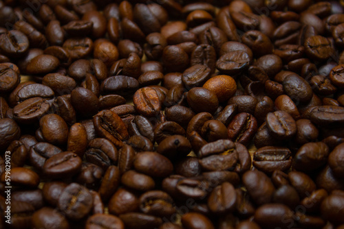 Fascinating background of roasted coffee beans. Fragrant roasted coffee beans are strewn on the table in a large layer. Beautiful background of coffee beans.
