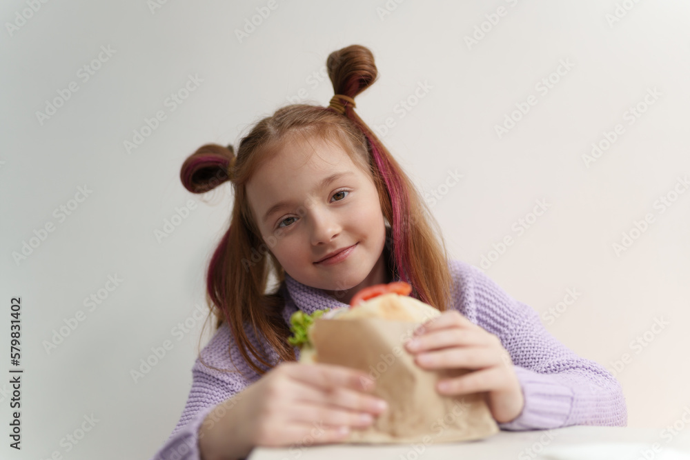 Cute little girl eats sandwich in fast food restaurant. Portrait of pretty white kid eating lunch meal in Greek cafe Cute little girl eats sandwich in fast food restaurant. Portrait of pretty white kid eating lunch meal in Greek cafe