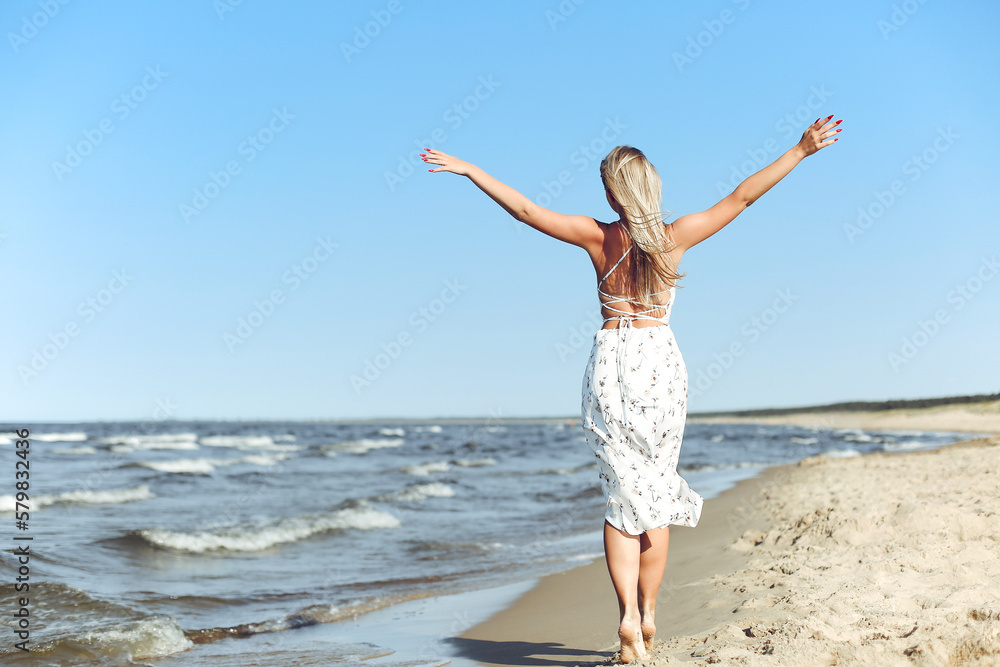 Happy blonde beautiful woman on the ocean beach standing in a white summer dress, open arms. Happy blonde beautiful woman on the ocean beach standing in a white summer dress, open arms.
