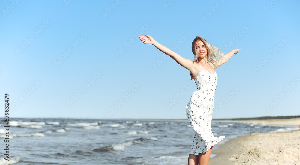 Happy blonde beautiful woman on the ocean beach standing in a white summer dress, open arms. Happy blonde beautiful woman on the ocean beach standing in a white summer dress, open arms.