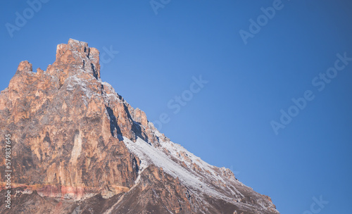 Massive rocky cliff of rocks of different colors with snow and a glacier in the light of the morning sun, a rocky peak in autumn with snow