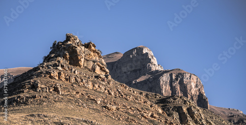 Rock formations protrude from a mountain and grassy hills on a sunny autumn morning