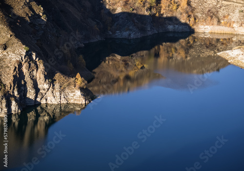 Rocky shore on the lake and reflection in the water in autumn at dawn, cliff break above the water