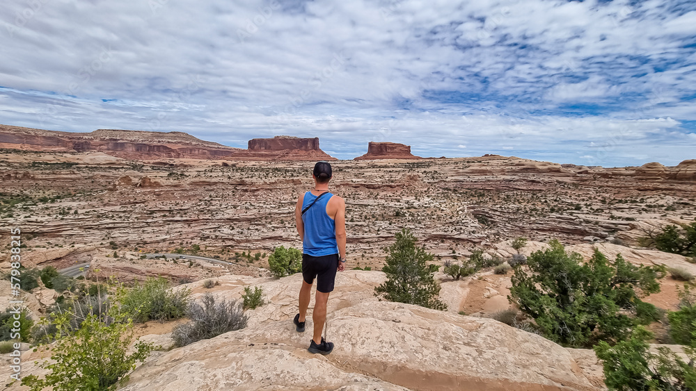 Man with panoramic view on Monitor and Merriamac Rock Formations near Moab, Canyonlands National Park, San Juan County, Utah, USA. Looking at natural pothole rock formation near Island in the Sky Mesa
