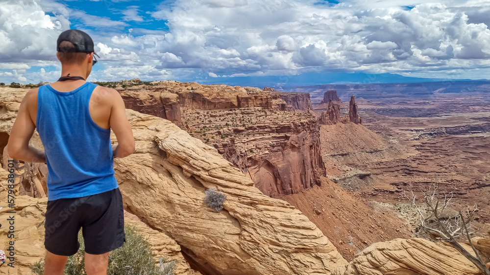 Fototapeta premium Man with panoramic view on Buck Canyon seen from Mesa Arch near Moab, Canyonlands National Park, San Juan County, Utah, USA. Looking at natural pothole arch rock formation near Island in the Sky Mesa