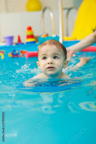 A 2-year-old little boy learns to swim in a pool with a coach. Swimming lessons for children