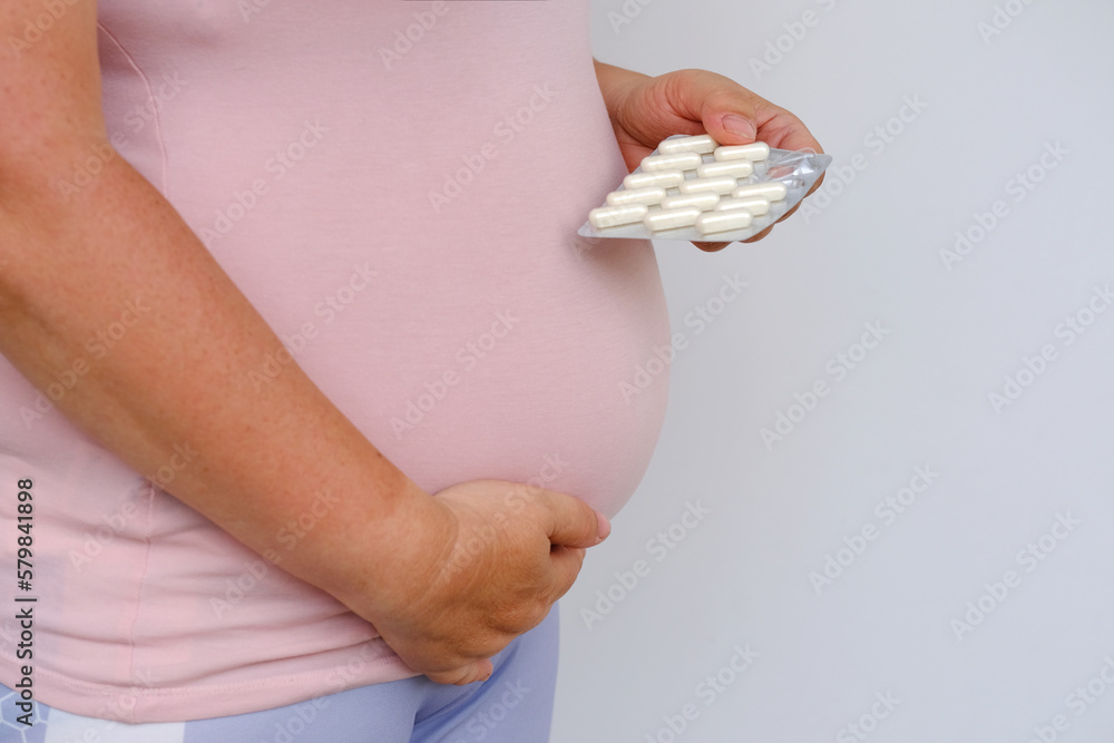 Obraz premium pregnant woman holds drugs, vitamins, hand on belly, concept influence of pharmacology on intrauterine development of fetus, vitamins for pregnant women, healthcare pregnancy, selective focus