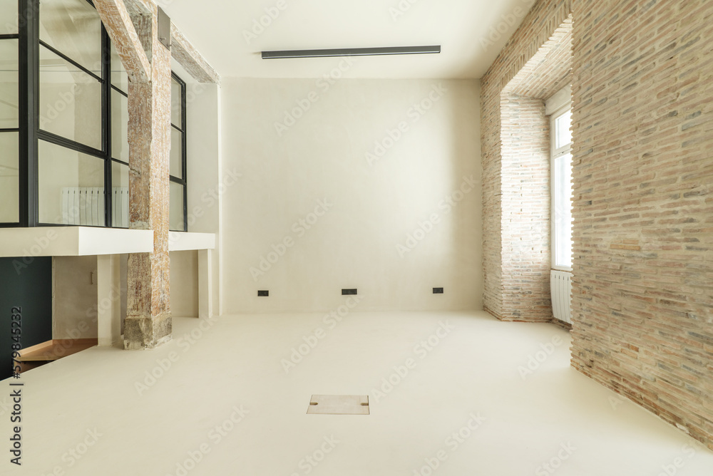 Obraz premium Empty room of a loft apartment with exposed brick walls, other smooth white walls and a room with glass partitions and black metal