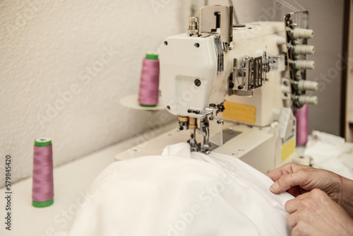 A female worker sewing white cloth with an electric sewing machine