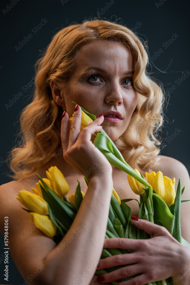 Portrait of candid authentic sexy model blonde girl half naked posing hugging bouquet of tulips