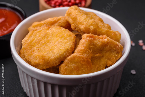 Delicious crispy chicken nuggets with salt and spices on a dark concrete background