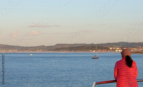 Woman in pink jacket looking at the horizon in a coastal landscape. © TopMicrobialStock