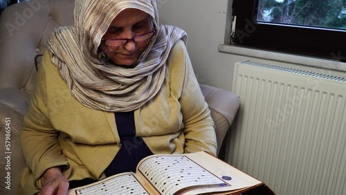 Old Muslim woman reading the Holy Quran at home during Ramadan Month. Old woman wearing white hijab reading the Koran.
