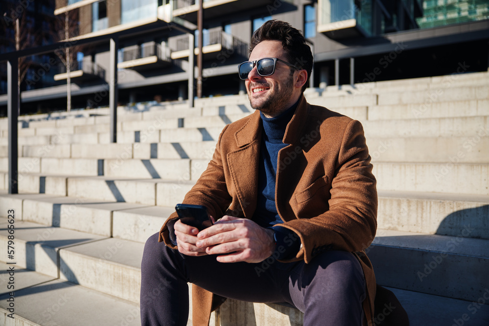 Handsome man enjoying sunny winter or spring day in the city relaxing on stairs Handsome man enjoying sunny winter or spring day in the city relaxing on stairs