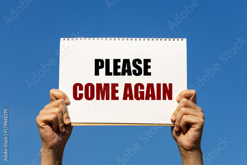 Please come again text on notebook paper held by 2 hands with isolated blue sky background. This message can be used as business concept to ask customer to visit us again. photo