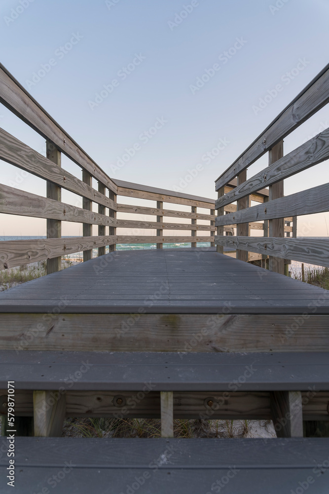 Footbridge with railings above sand dunes on a beach in Destin, Florida. Vertical shot view of a wooden pathway against the horizon skyline. Footbridge with railings above sand dunes on a beach in Destin, Florida. Vertical shot view of a wooden pathway against the horizon skyline.