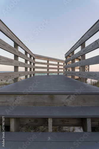 Footbridge with railings above sand dunes on a beach in Destin, Florida. Vertical shot view of a wooden pathway against the horizon skyline.