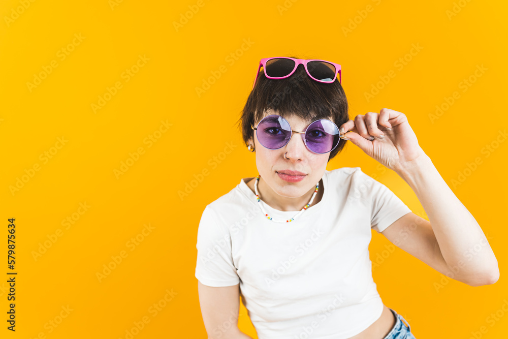 Femal model looking directly into the camera through a pair of sunglasses and wearing another pair on her head. Bright orange background. Medium shot. High quality photo Femal model looking directly into the camera through a pair of sunglasses and wearing another pair on her head. Bright orange background. Medium shot. High quality photo