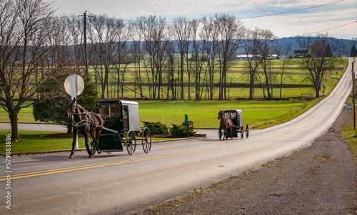A View of Two Amish Horse and Buggies Traveling Down a Countryside Road Thru Farmlands on a Sunny December Day photo