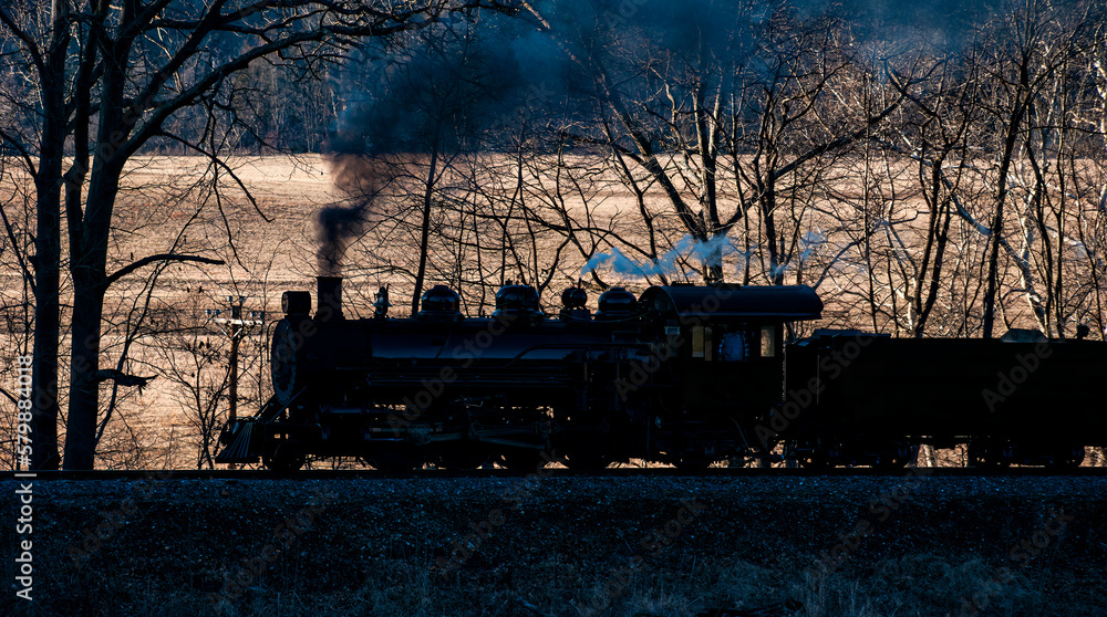 A Sunset View of a Narrow Gauge Restored Steam Passenger Train Blowing Smoke and Traveling Thru Farmlands on a Winter Day
