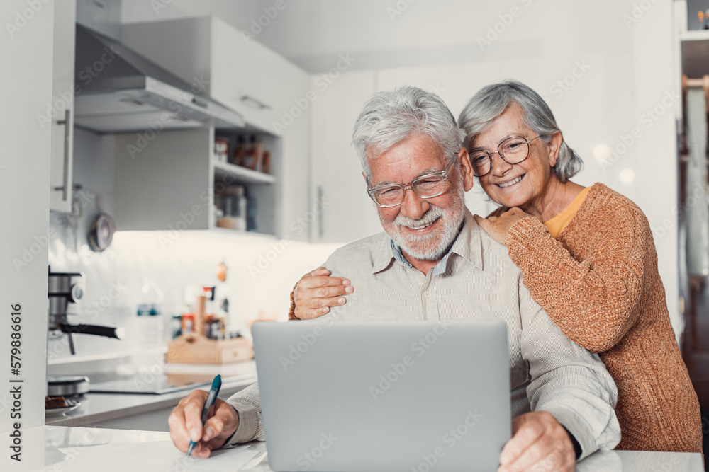 Old age and modern tech. Retired family couple sit at kitchen table use laptop watch photo video read latest news online. Aged husband share discuss interesting information on website with senior wife Old age and modern tech. Retired family couple sit at kitchen table use laptop watch photo video read latest news online. Aged husband share discuss interesting information on website with senior wife