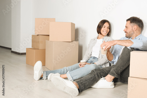 Happy couple with takeaway coffee resting on floor in new apartment. Moving day