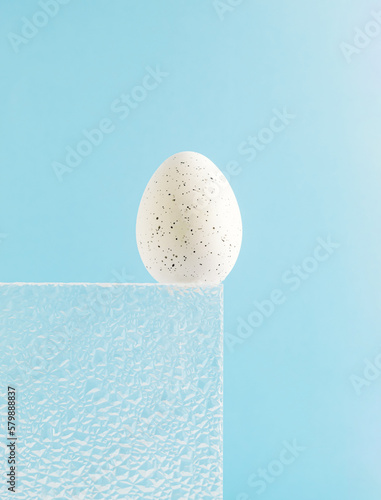 Trendy composition made of white Easter egg on sky blue background. Embossed glass texture background. Minimal festive concept. Abstract Easter card. Copy space.