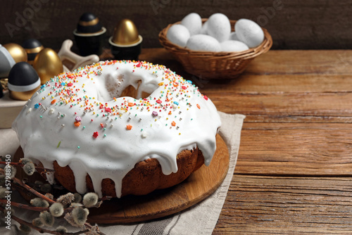 Delicious Easter cake decorated with sprinkles near painted eggs and willow branches on wooden table. Space for text photo