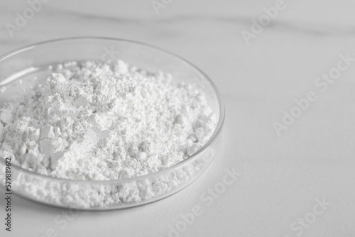 Petri dish with calcium carbonate powder on white marble table, closeup. Space for text