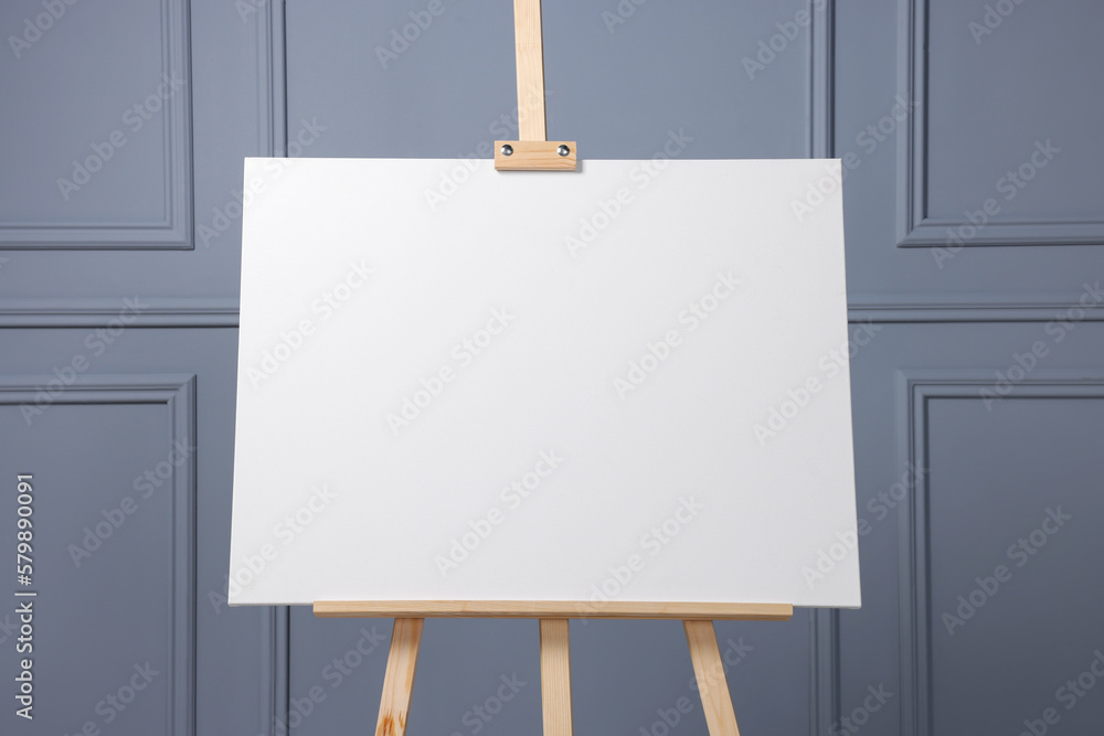 Wooden easel with blank canvas near grey wall indoors, closeup. Space for text Wooden easel with blank canvas near grey wall indoors, closeup. Space for text