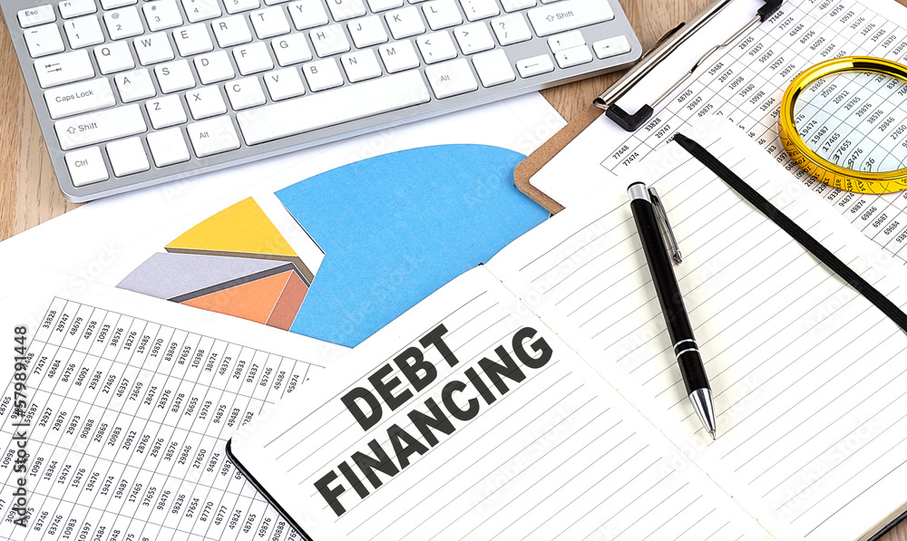 DEBT FINANCING text on notebook with chart and keyboard DEBT FINANCING text on notebook with chart and keyboard
